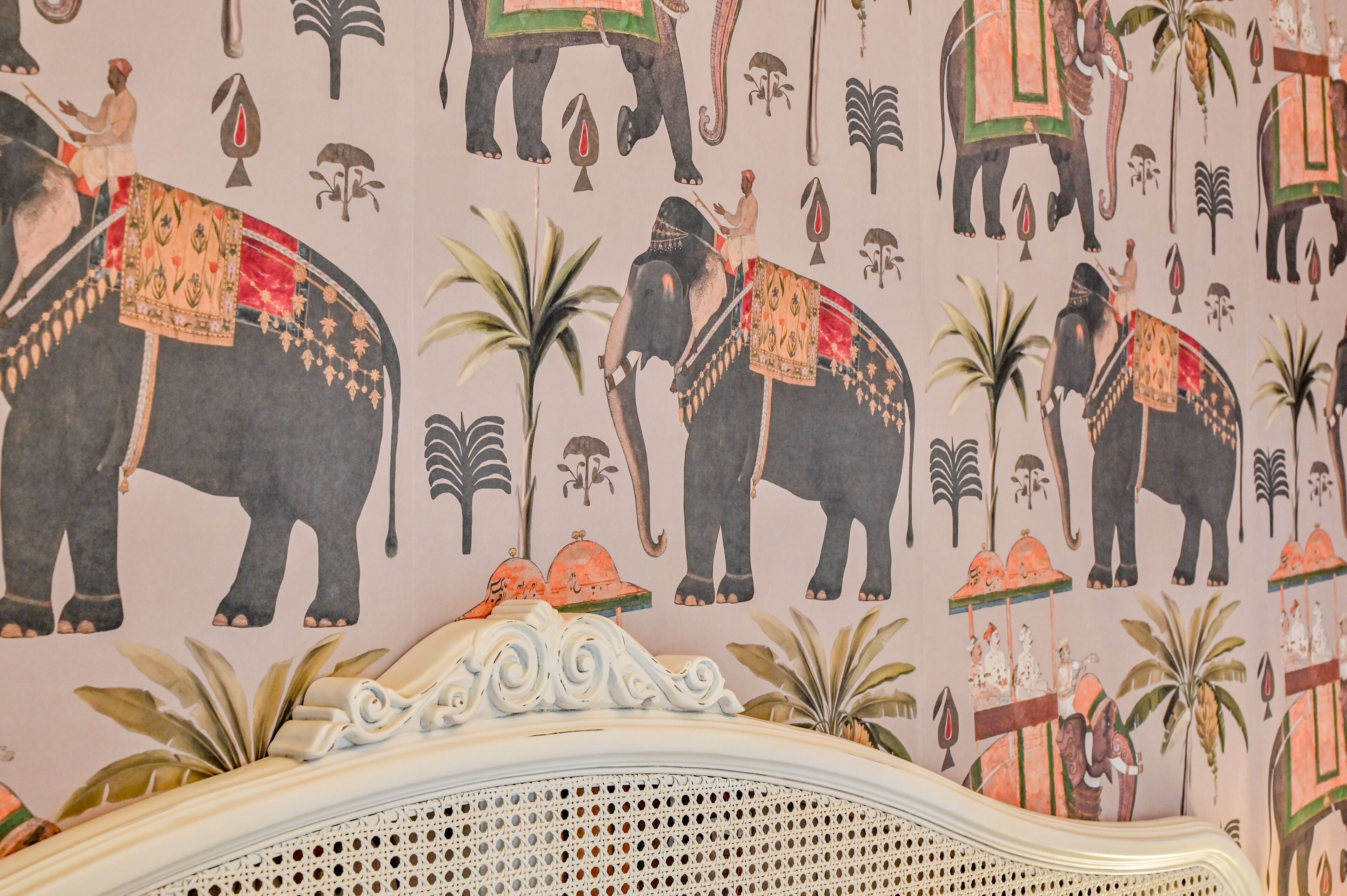 A wall with elephant and palm tree patterns, a bed with a white headboard, and a decorative ceiling.