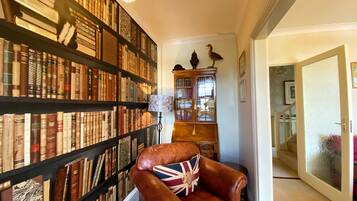 Eine Bibliothek mit Bücherregalen, einem Ledersessel mit Union-Jack-Kissen und einer Holzkabine mit Glastüren.