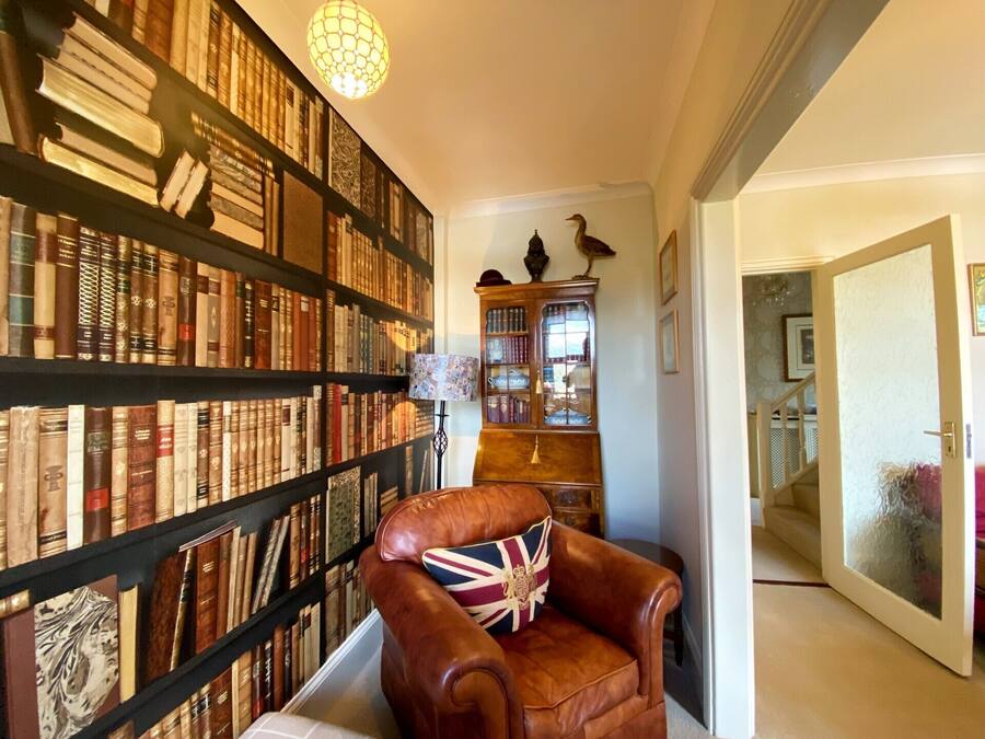 Eine Bibliothek mit Bücherregalen, einem Ledersessel mit Union-Jack-Kissen und einer Holzkabine mit Glastüren.
