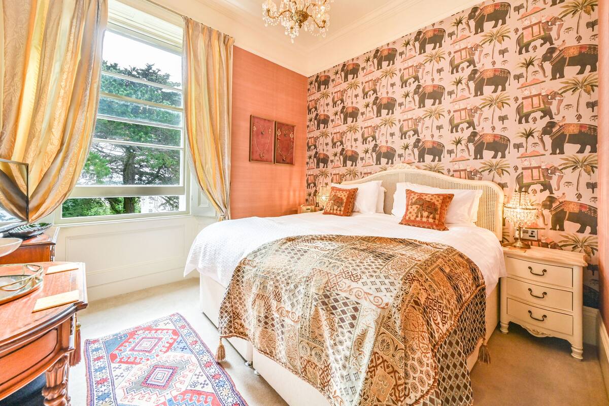 A bedroom with a large bed, a nightstand, a dresser, and a window with curtains.