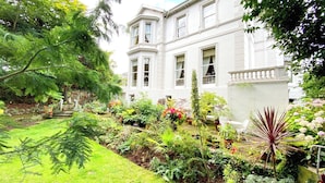 Un edificio blanco con numerosas ventanas y un jardín con diversas plantas y un pequeño estanque.