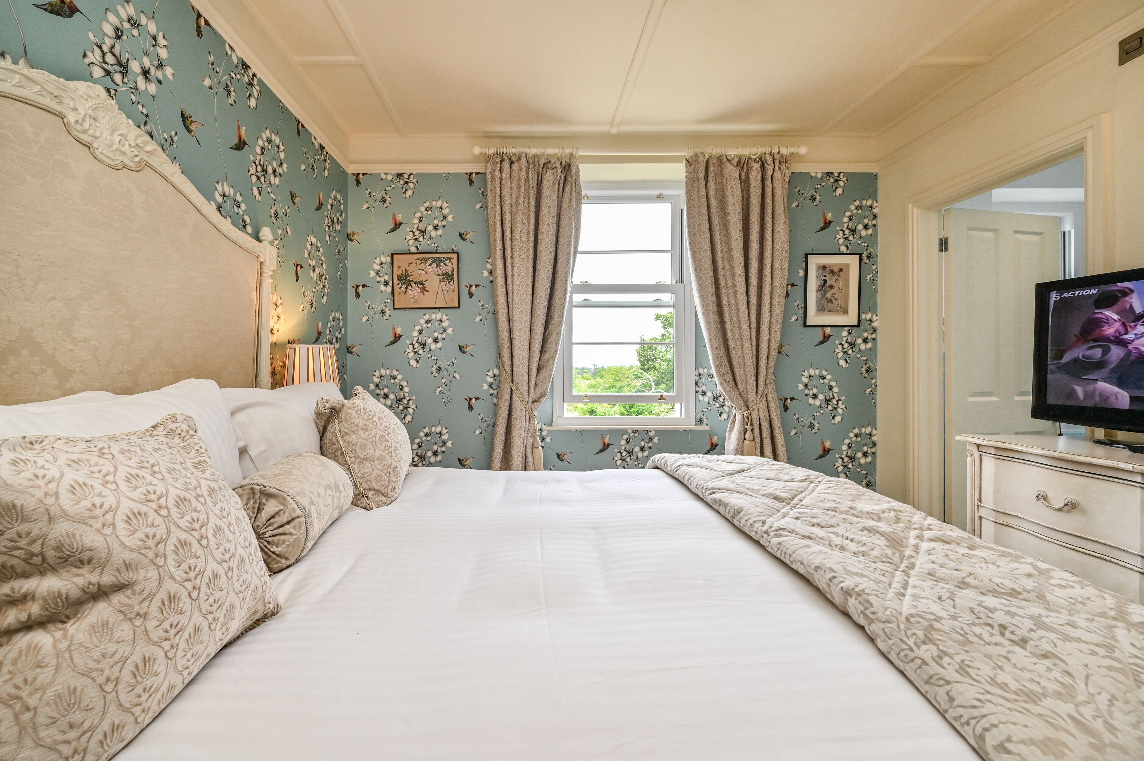 Een slaapkamer met een groot bed, een televisie en een raam met gordijnen.