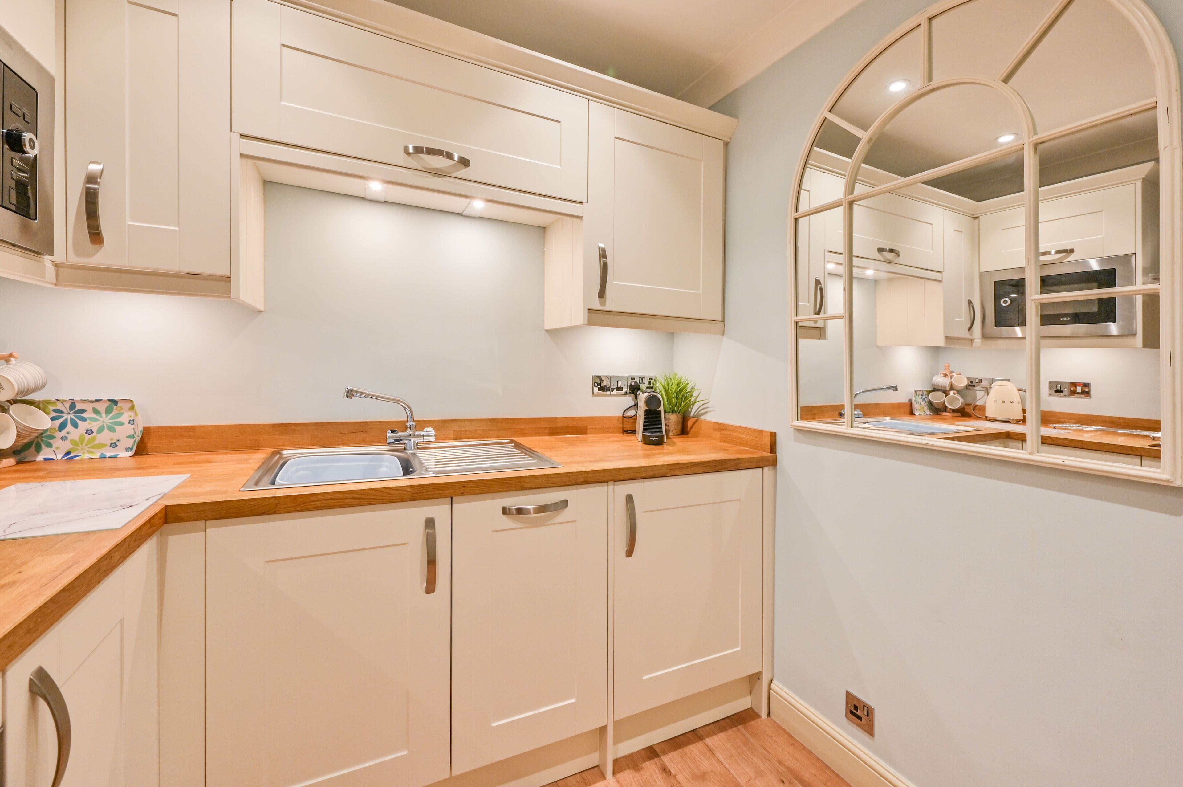 A modern kitchen with white cabinets, a wooden countertop, and a stainless steel sink.