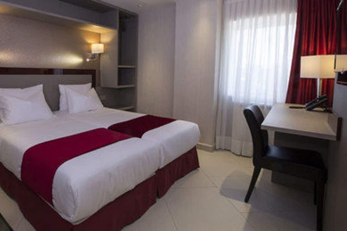 Une chambre d’hôtel avec un lit double, deux tables de chevet, un bureau avec une chaise et une fenêtre avec des rideaux.