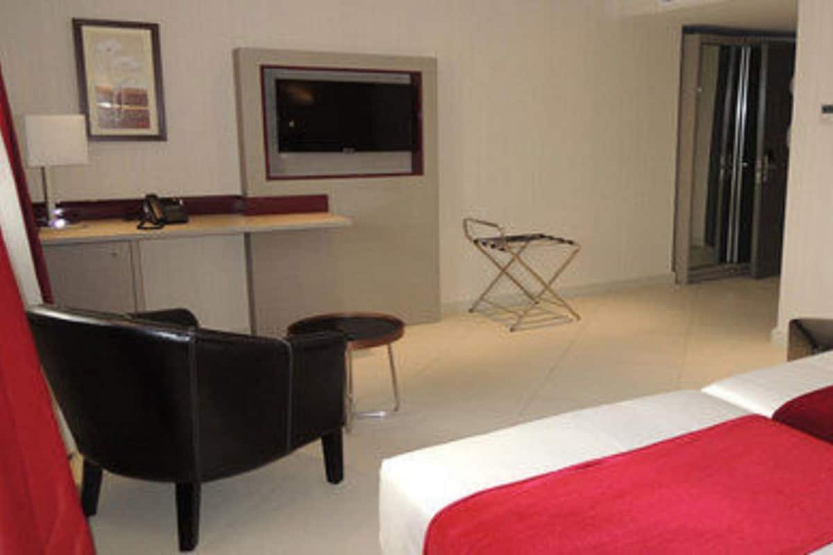 Une chambre d’hôtel avec un lit, un bureau, une chaise, une télévision et une porte.