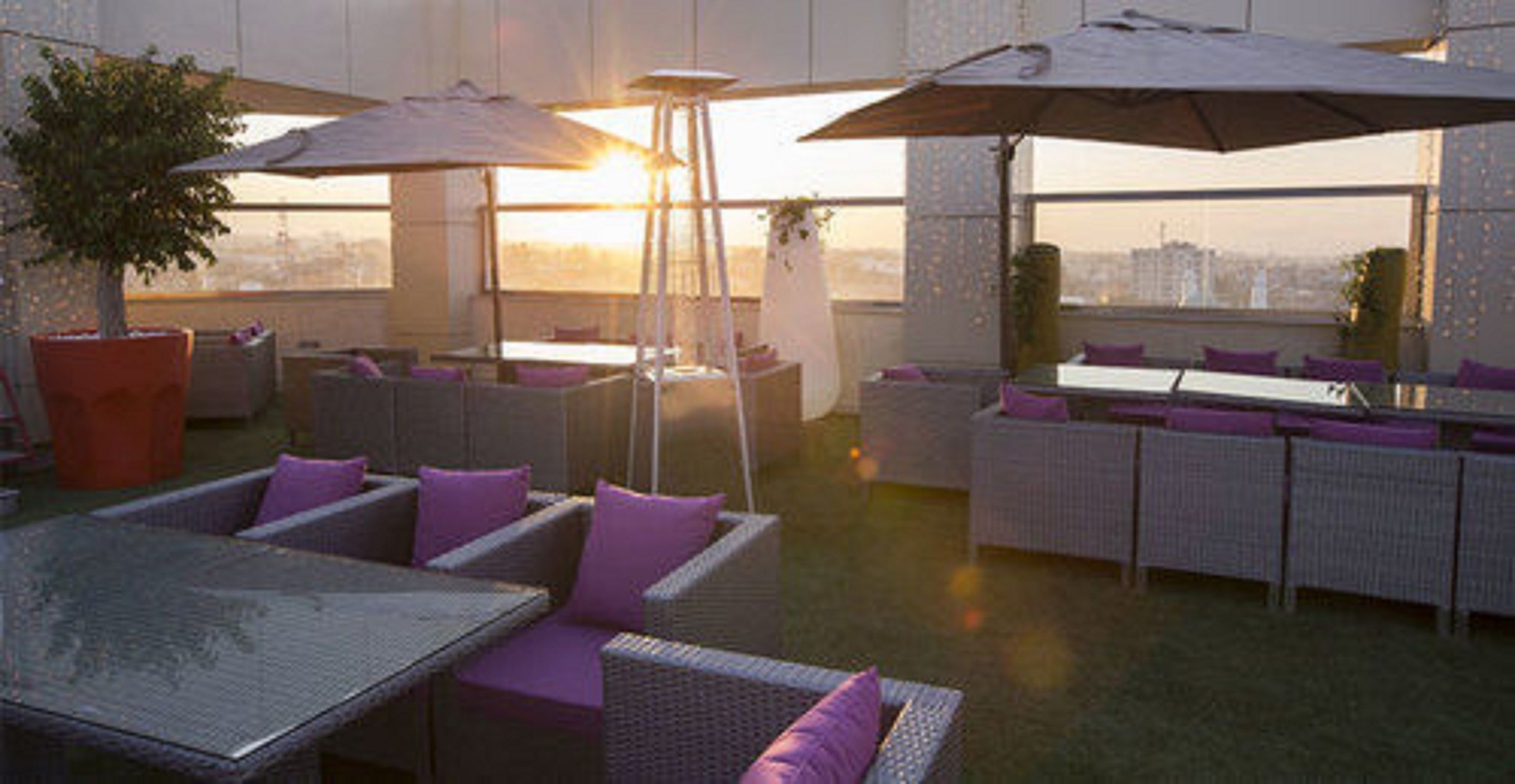 An outdoor seating area with wicker furniture and umbrellas, overlooking a cityscape.