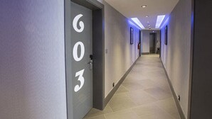 A hallway with a door labeled '603' leading to a room. The hallway has a tiled floor and is illuminated by overhead lighting. - KT Hotels (Ouled Yaich)