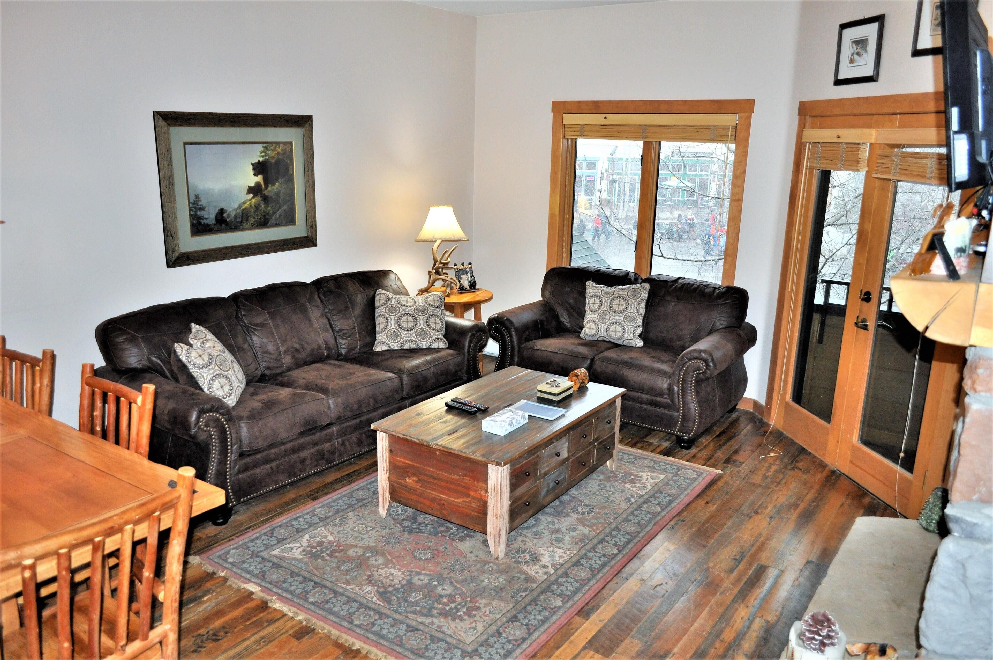 A living room with two leather sofas, a wooden coffee table, a dining table with chairs, a patterned rug, and a framed picture on the wall.