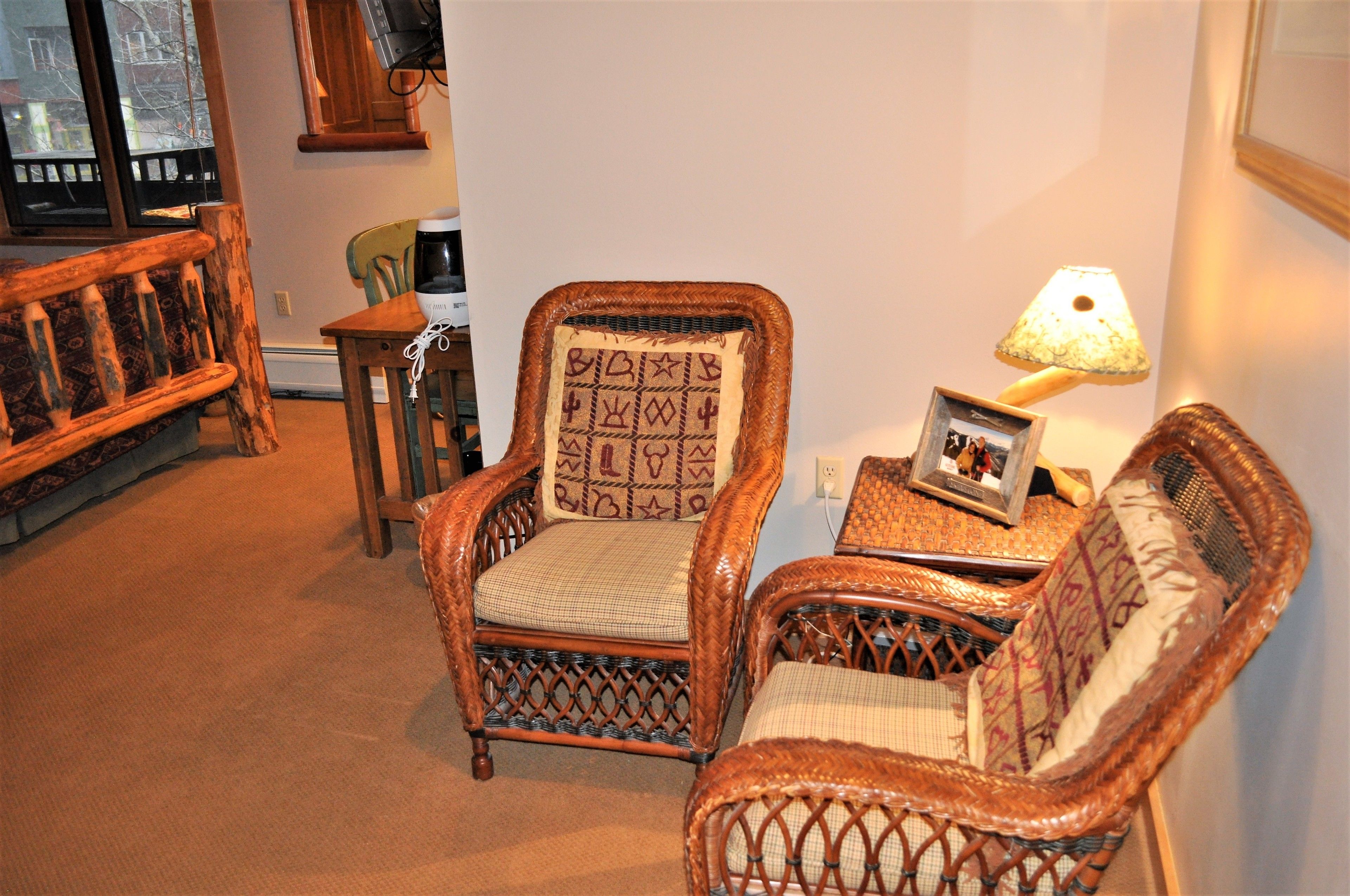 A cozy living room with wicker furniture, a coffee table with a picture frame, and a lamp.