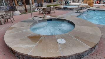 Un jacuzzi con revestimiento de piedra, una piscina y mobiliario exterior.