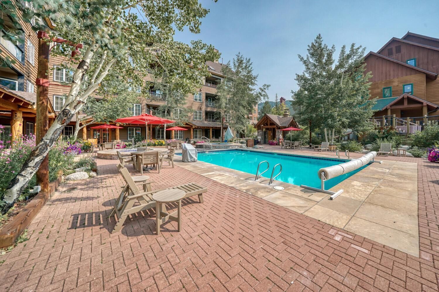 A pool area with lounge chairs and umbrellas, surrounded by buildings with balconies and wooden exteriors.