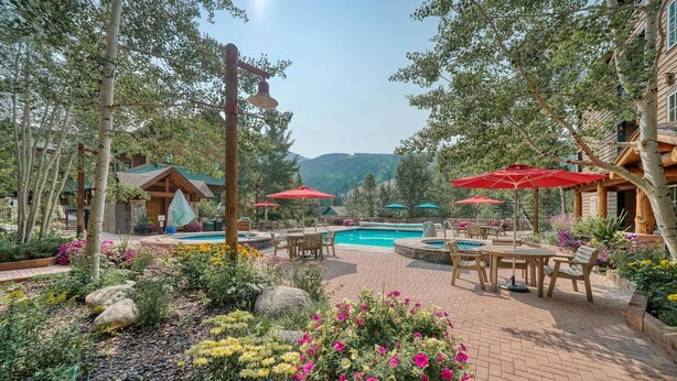 A pool area with outdoor seating and umbrellas, surrounded by trees and flowers. - Buffalo Lodge 3 Bed 3 Bath (Keystone)