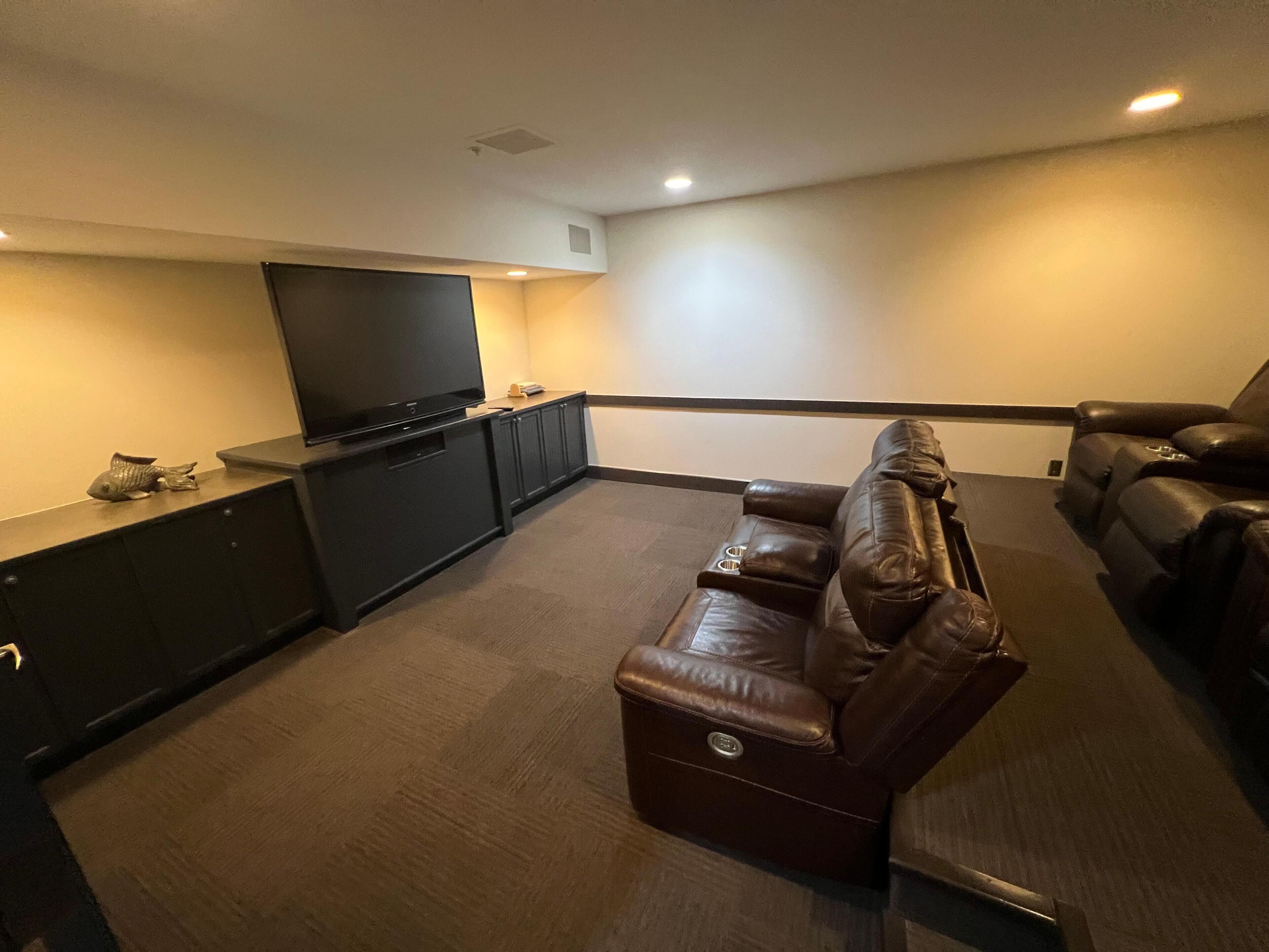 A home theater room with a large flat-screen TV, dark leather recliner, and a dark entertainment unit.