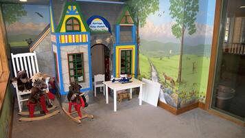 Una sala de juegos infantil con un mural de un paisaje, una casita de juegos y un caballo balancín.
