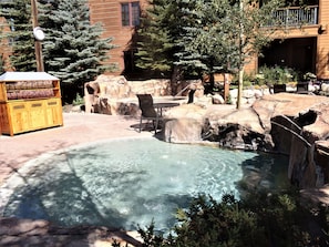 A clear pool with a rock feature, a wooden bench, and a trash bin labeled 'TOWELS' and 'TRASH'. - Springs 2 Bed 3 Bath Murphy (Keystone)