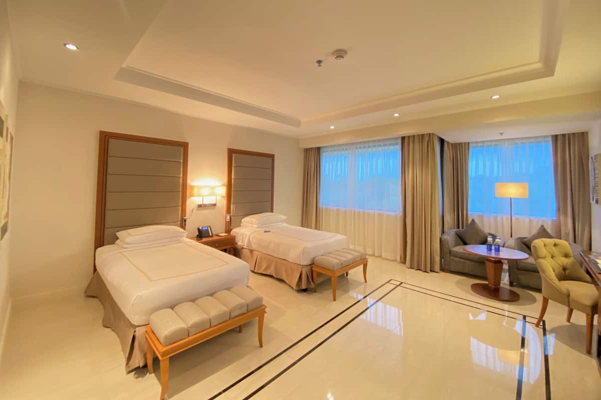 A hotel room with two beds, a sofa, a small table, and a chair.
