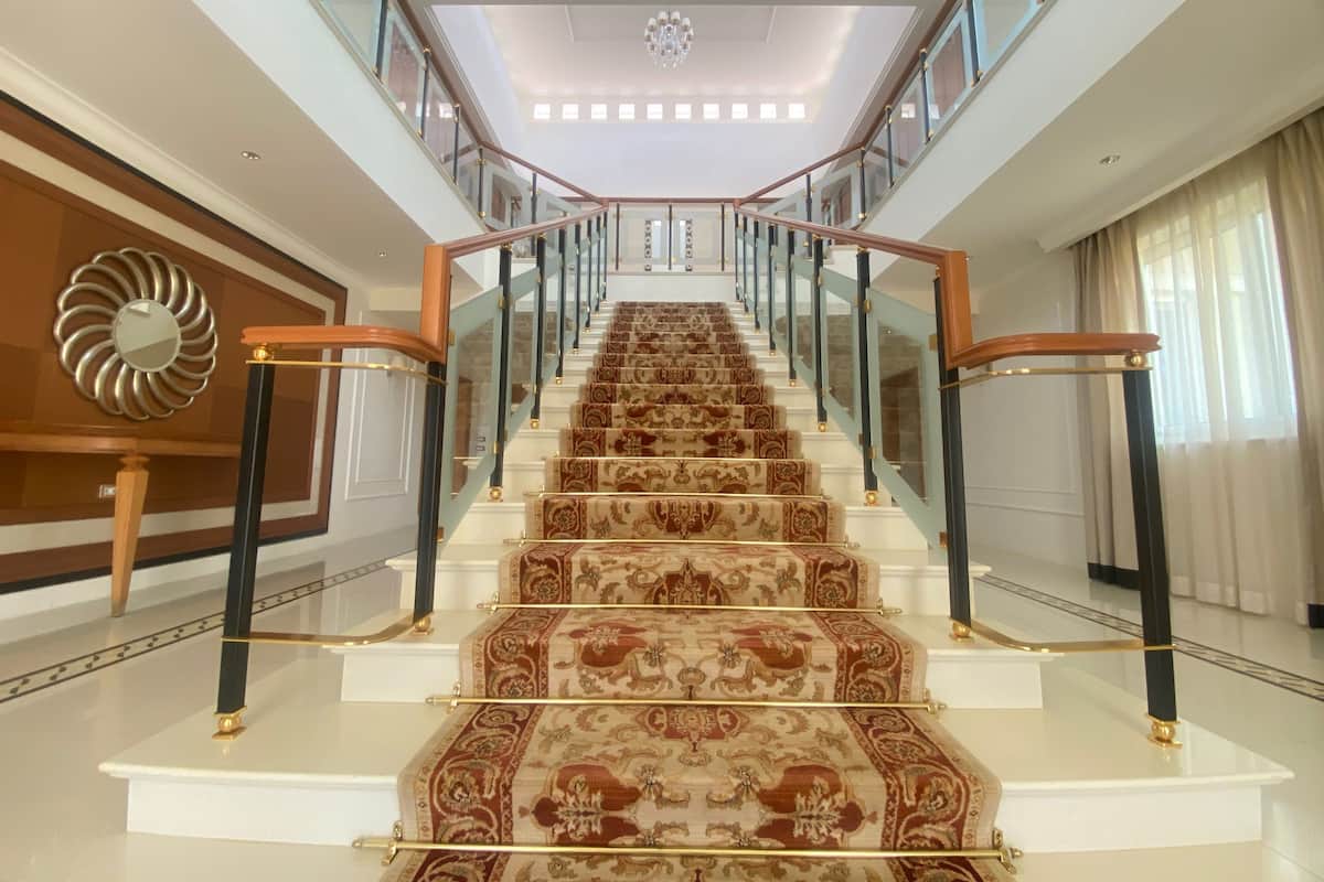A grand staircase with ornate carpeted steps, glass railings, and a chandelier.