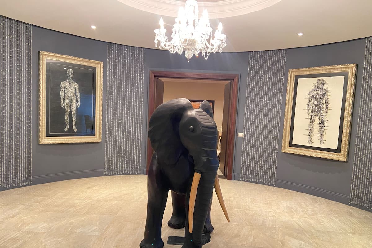 A room with a large elephant sculpture, framed artwork on the walls, a chandelier, and a wooden floor.