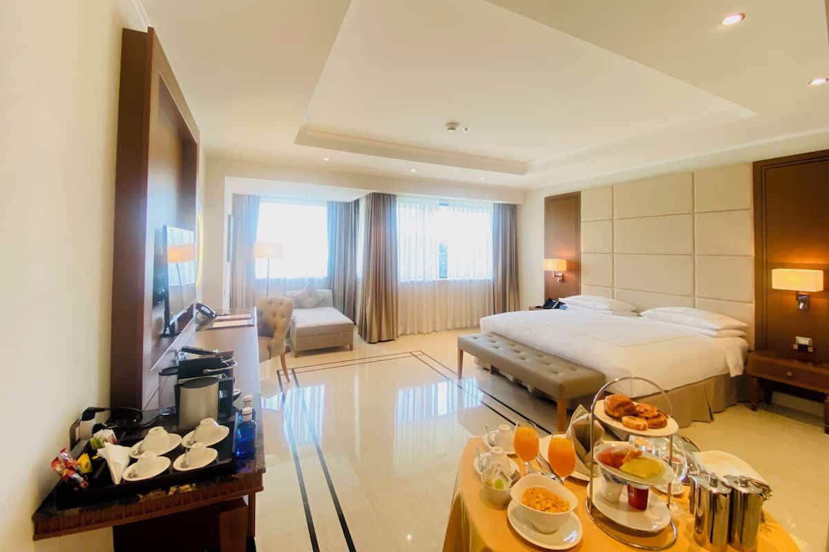 A hotel room with a large bed, a bedside table with breakfast items, a desk with a chair, and a view of the room's interior.