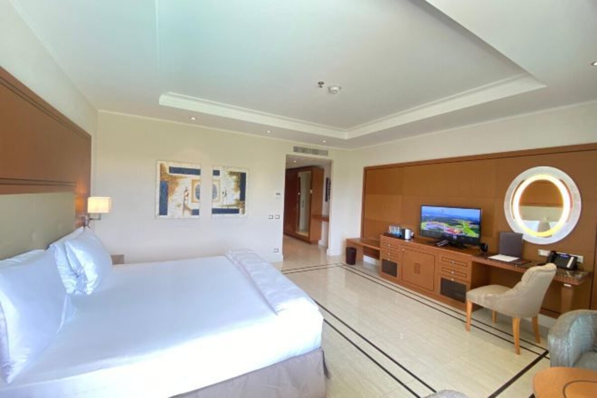 Quarto de hotel com uma cama grande, uma escrivaninha com computador, televisão e espelho.