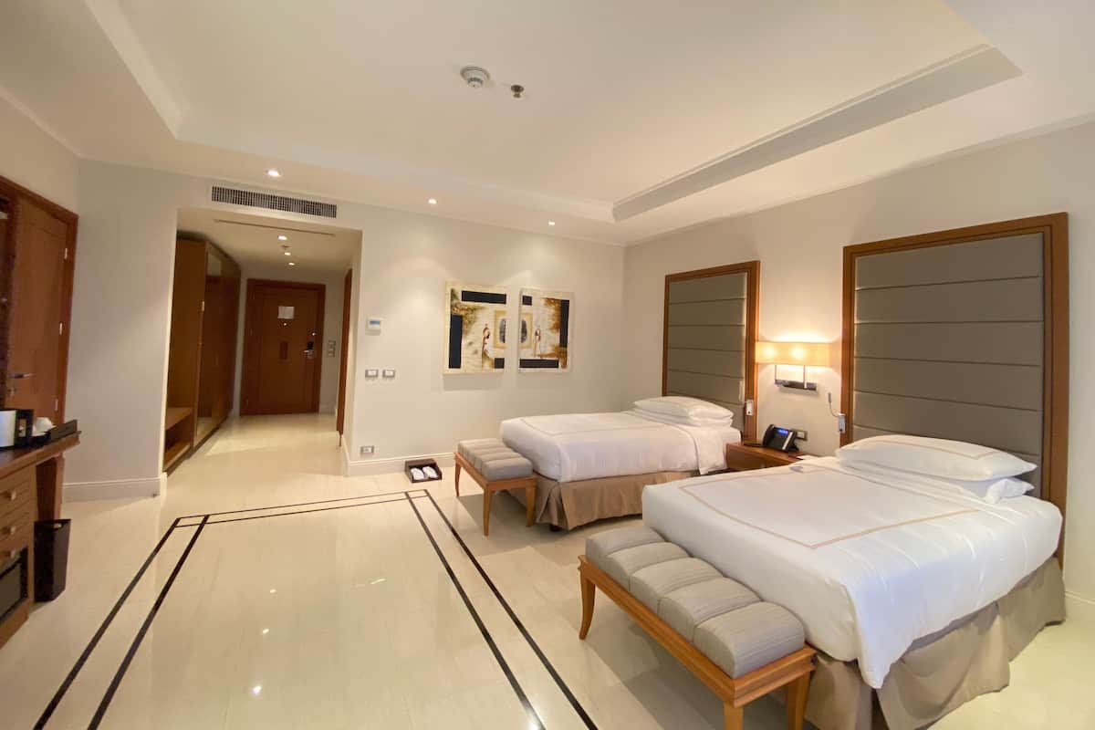 A hotel room with two beds, a bench, a wardrobe, and a bathroom.