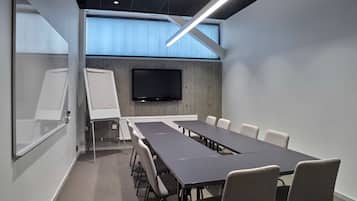 A conference room with a long table, chairs, a whiteboard, and a flat-screen TV on the wall.