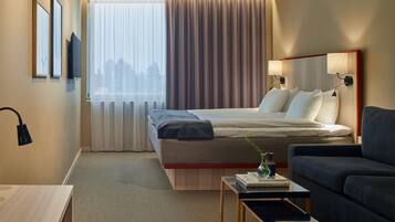 Una habitación de hotel con cama, sofá, una mesita y una ventana con cortinas.