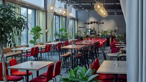 A spacious indoor dining area with multiple tables and chairs, large windows, and hanging pendant lights.