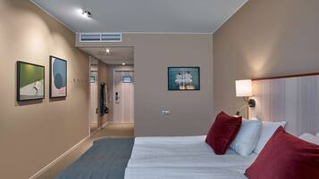 A hotel room with a bed, a nightstand, a wall-mounted lamp, and a framed picture on the wall.