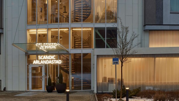 A modern building with a glass facade, a spiral staircase, and a sign reading "SCANDIC ARLANDASTAD."