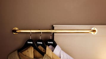 A brass curtain rod with three black hangers labeled "Scandic" against a beige wall.
