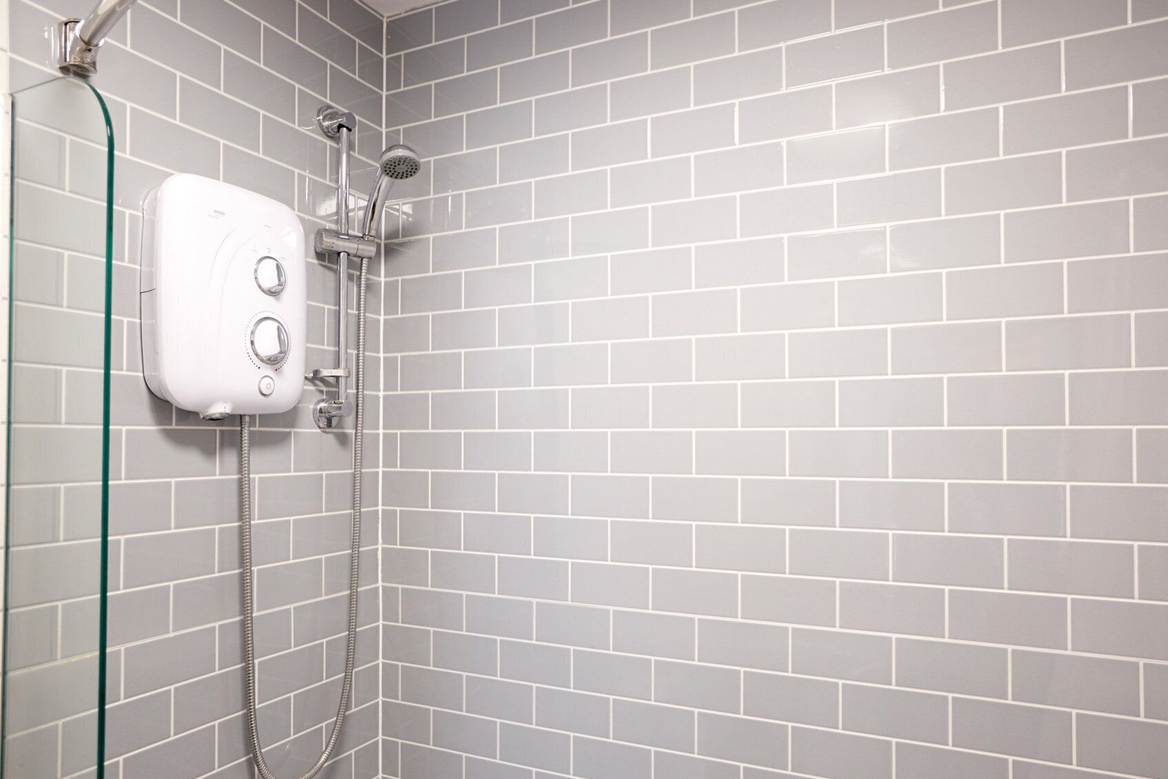 A shower with a handheld showerhead and a wall-mounted control panel.