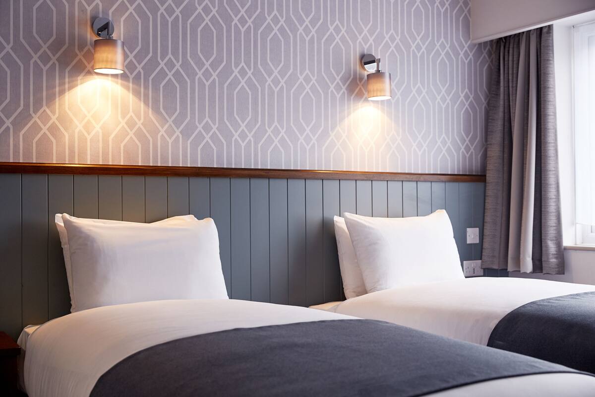 Een hotelkamer met twee bedden, een houten hoofdbord en behang met een patroon.