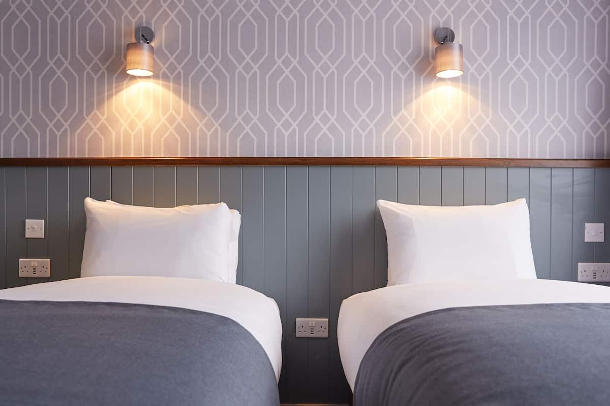 Een hotelkamer met twee bedden, een houten hoofdbord en een behang met een patroon.