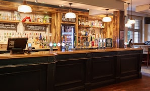 A bar area with a wooden counter, multiple beer taps, and a variety of liquor bottles. - The Chase Hotel by Greene King Inns (Nuneaton)
