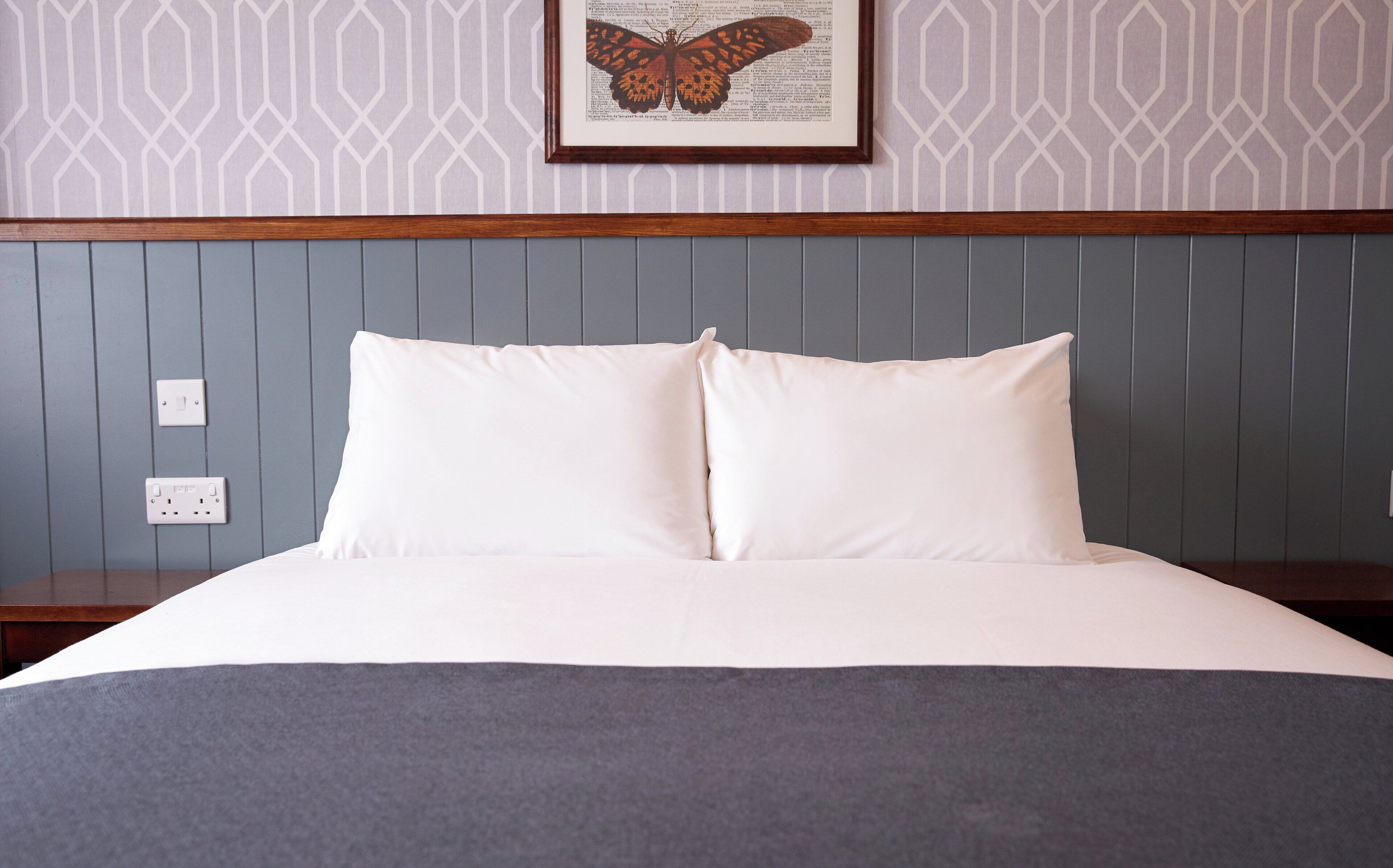 A neatly made bed with white linens, a gray throw blanket, and a framed butterfly artwork above it.
