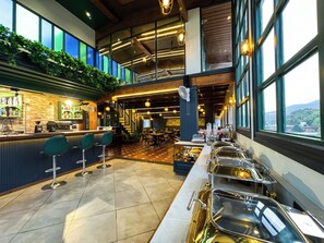 Zona de bar moderna con mostrador, taburetes y un espacio tipo buffet con fuentes de servicio.