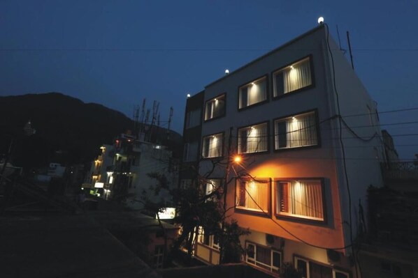 Un edificio de varios pisos con ventanas iluminadas durante la noche, rodeado de otras construcciones.