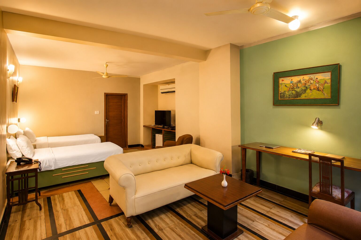 Habitación de hotel con sofá, dos camas individuales, televisión, escritorio y un cuadro en la pared.