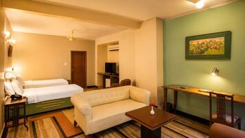 Habitación de hotel con sofá, dos camas individuales, televisión, escritorio y un cuadro en la pared.