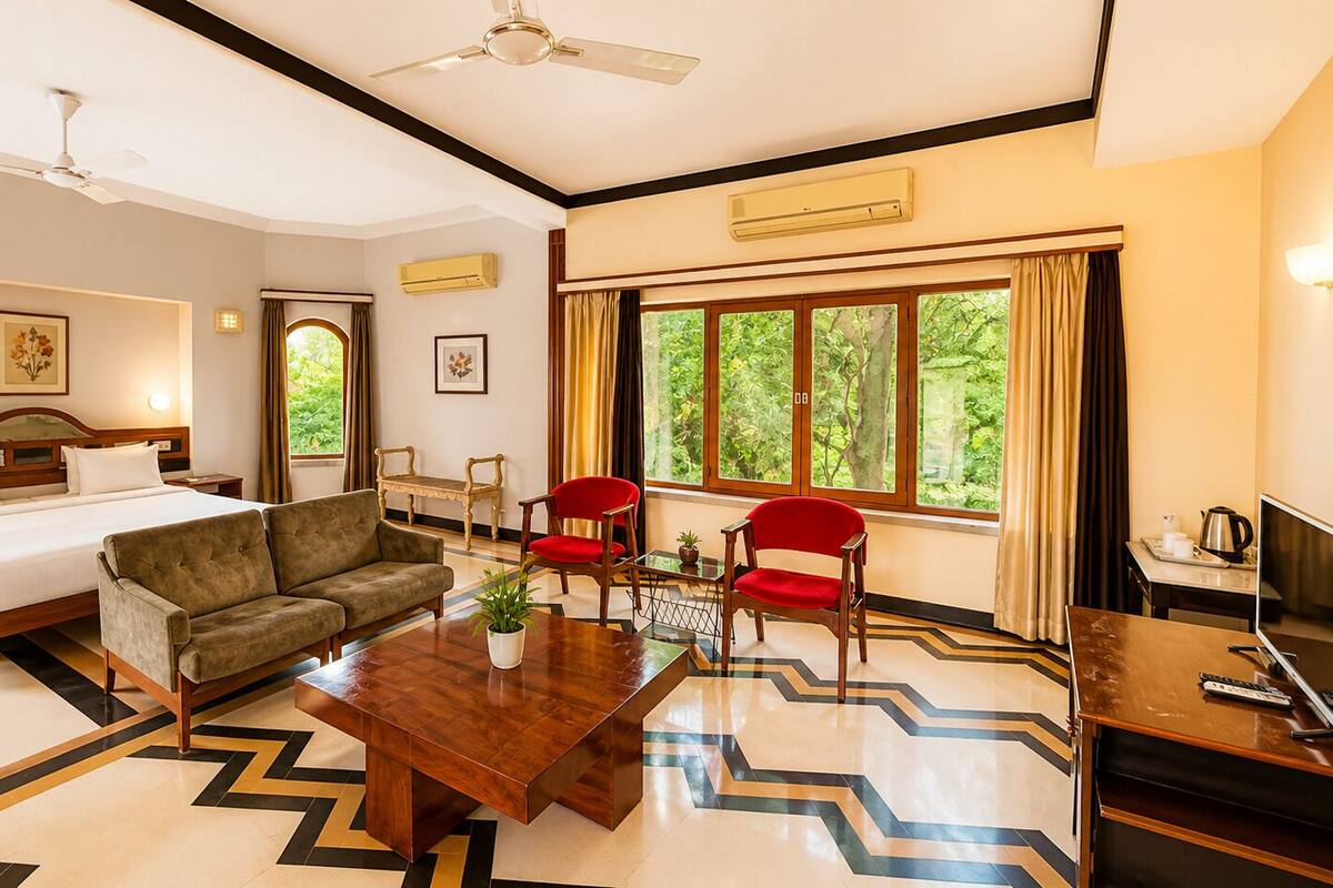 A hotel room with a bed, sofa, chairs, a coffee table, a TV, and large windows.