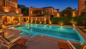 A swimming pool with lounge chairs, a stone building, and a hedge in the background. - Hotel Inn Season - A Heritage Hotel in Jodhpur (Jodhpur)