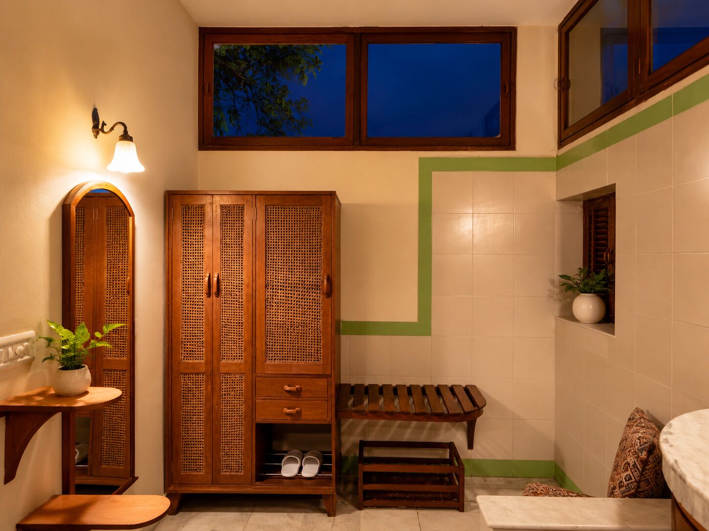 Een badkamer met een houten garderobe, een bankje, een tafeltje met een plant en een raam met uitzicht op bomen.