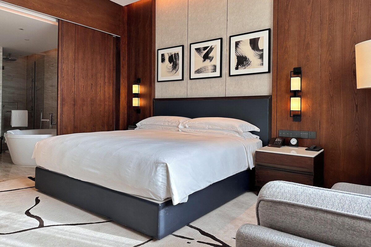 A modern hotel room with a large bed, wooden paneling, and artwork on the wall.