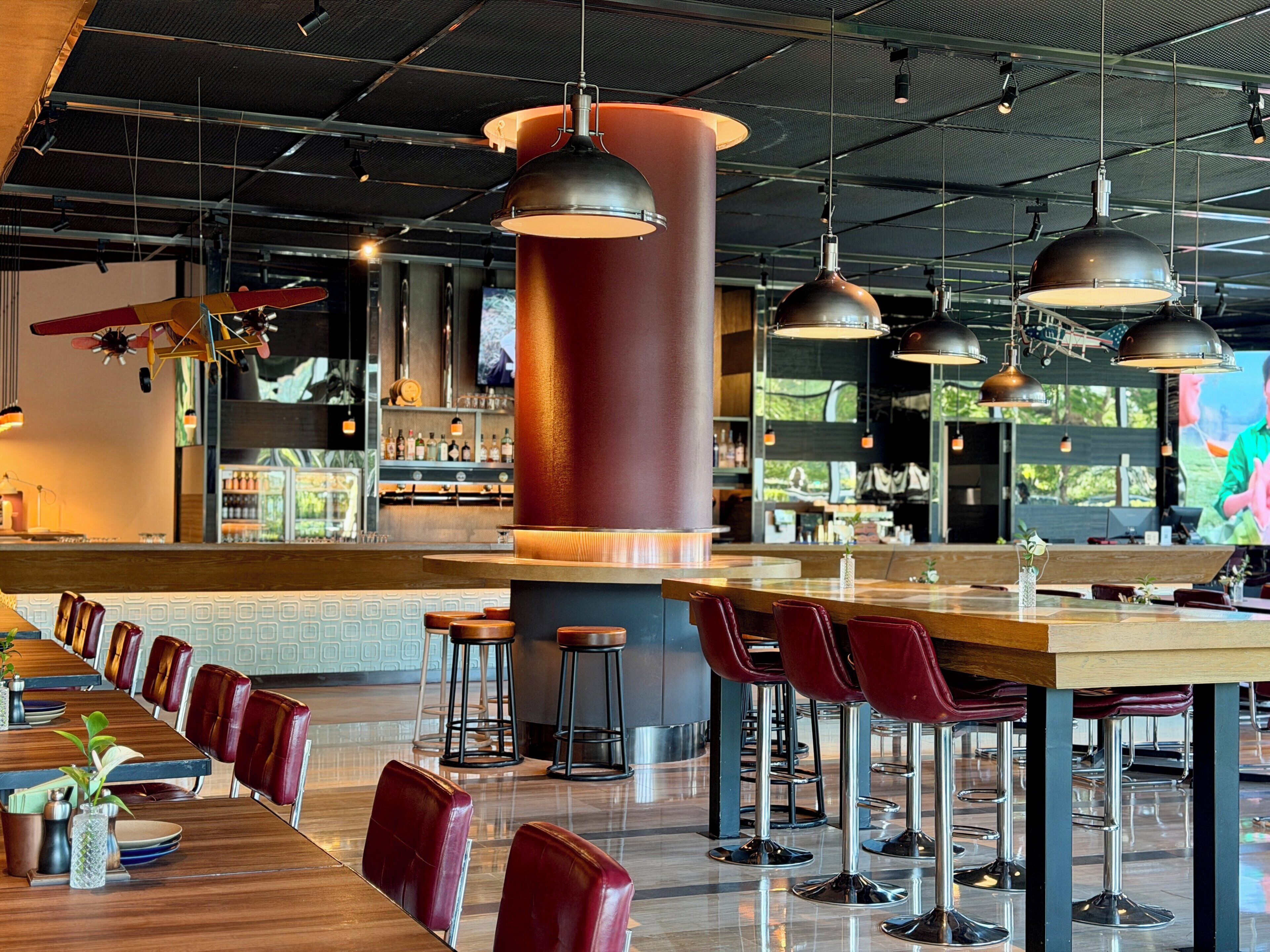 Un área de bar moderna con taburetes altos, una barra alargada e iluminación colgante.