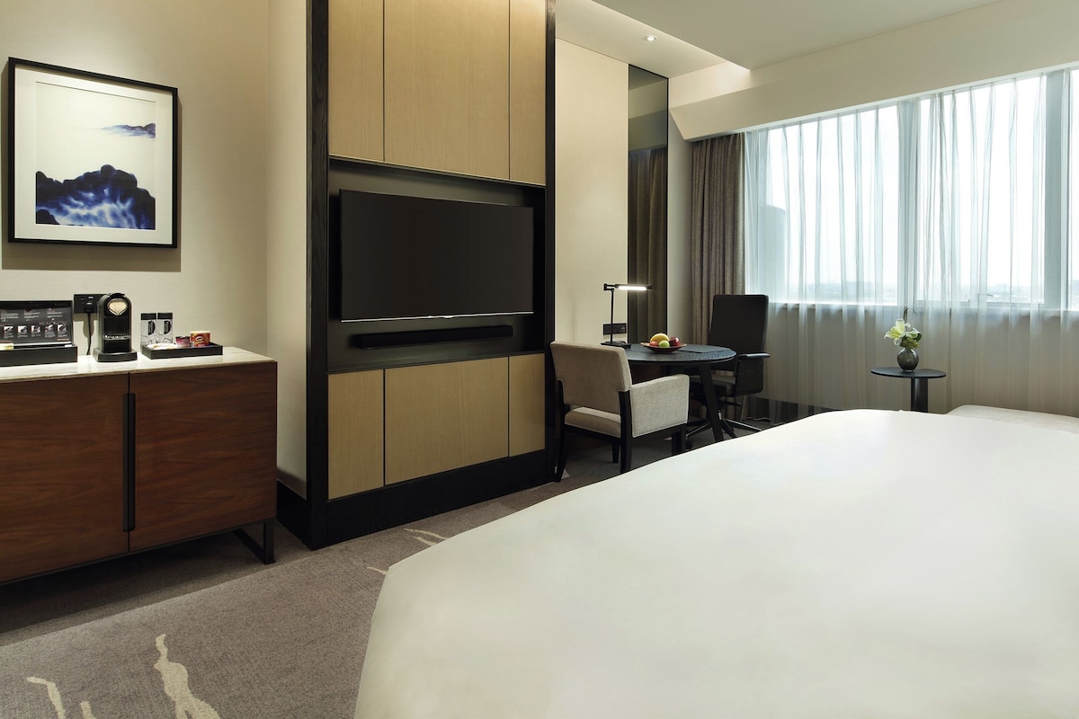 Una habitación de hotel con una cama grande, un escritorio con silla, televisor y cafetera.
