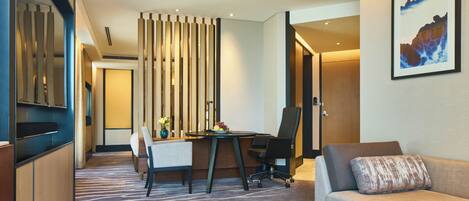 A hotel room with a dining area, a sofa, a painting, and a view of the city.