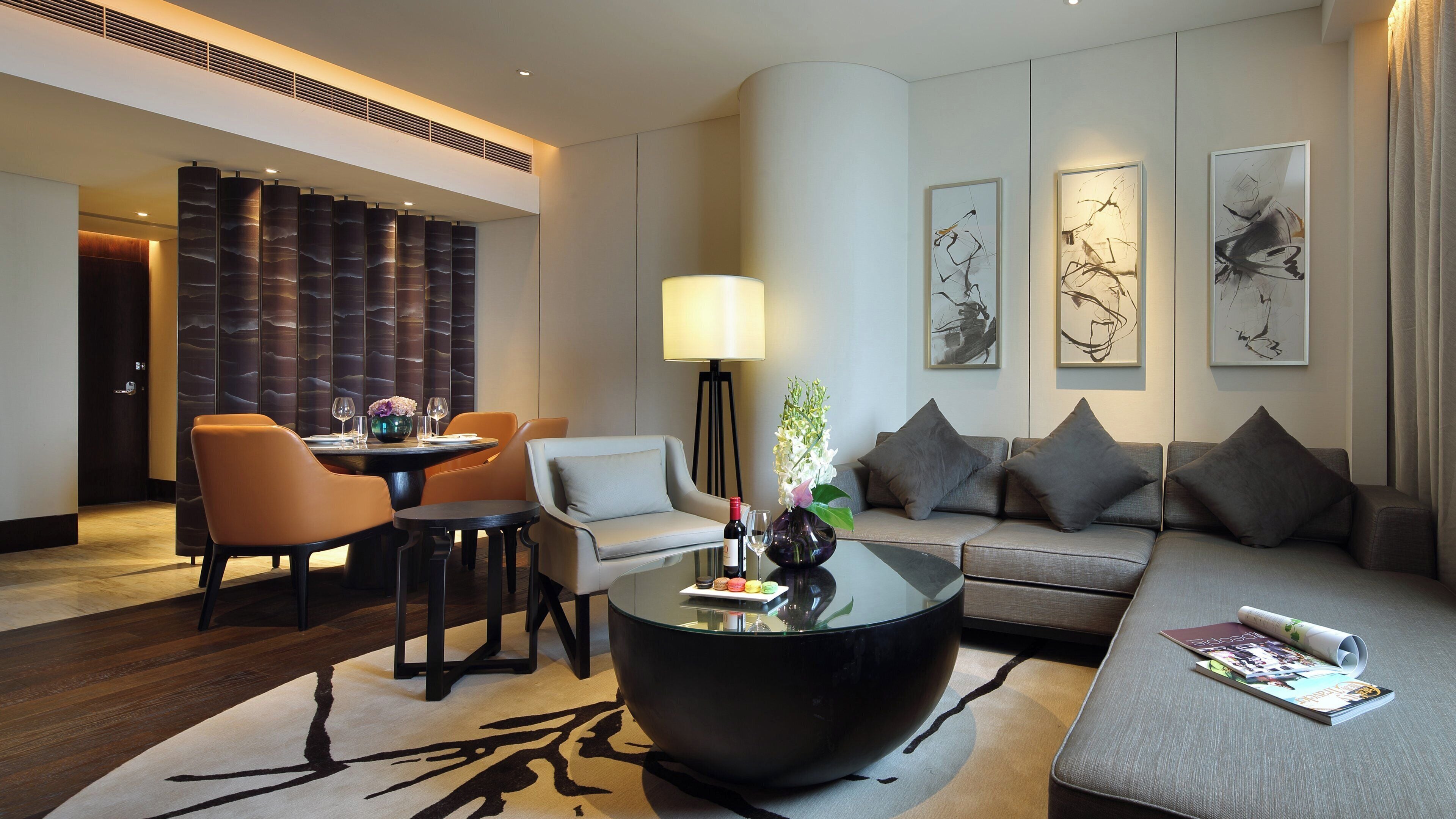 Ein modernes Hotelzimmer mit Essbereich, einer Sitzecke, einem Couchtisch und Kunstwerken an den Wänden.