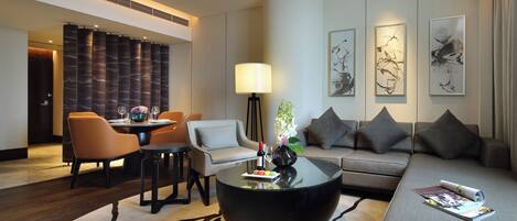 Ein modernes Hotelzimmer mit Essbereich, einer Sitzecke, einem Couchtisch und Kunstwerken an den Wänden.