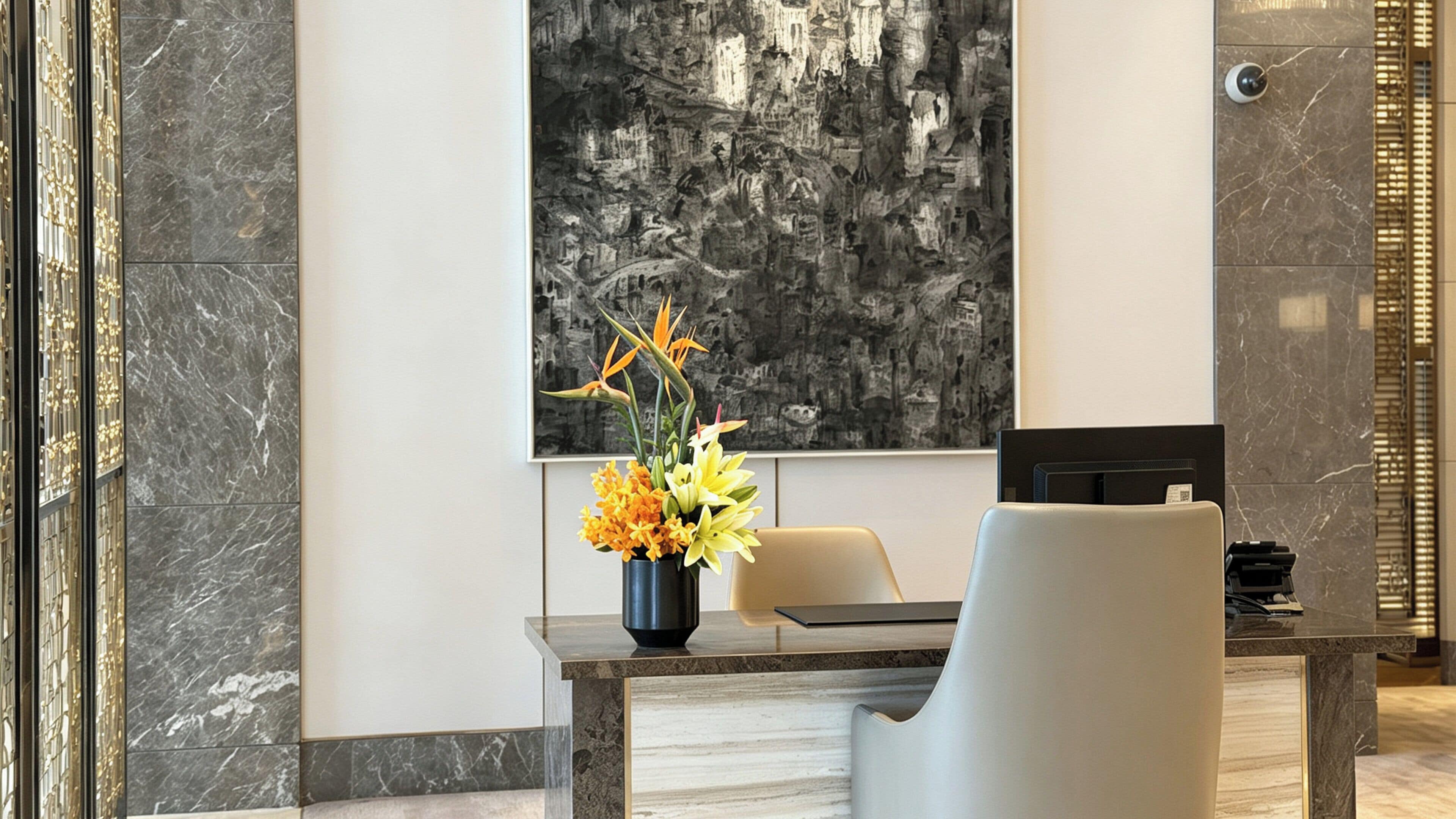 Un interior moderno con una pared de mármol, un cuadro abstracto grande, un escritorio con una silla y un jarrón de flores.